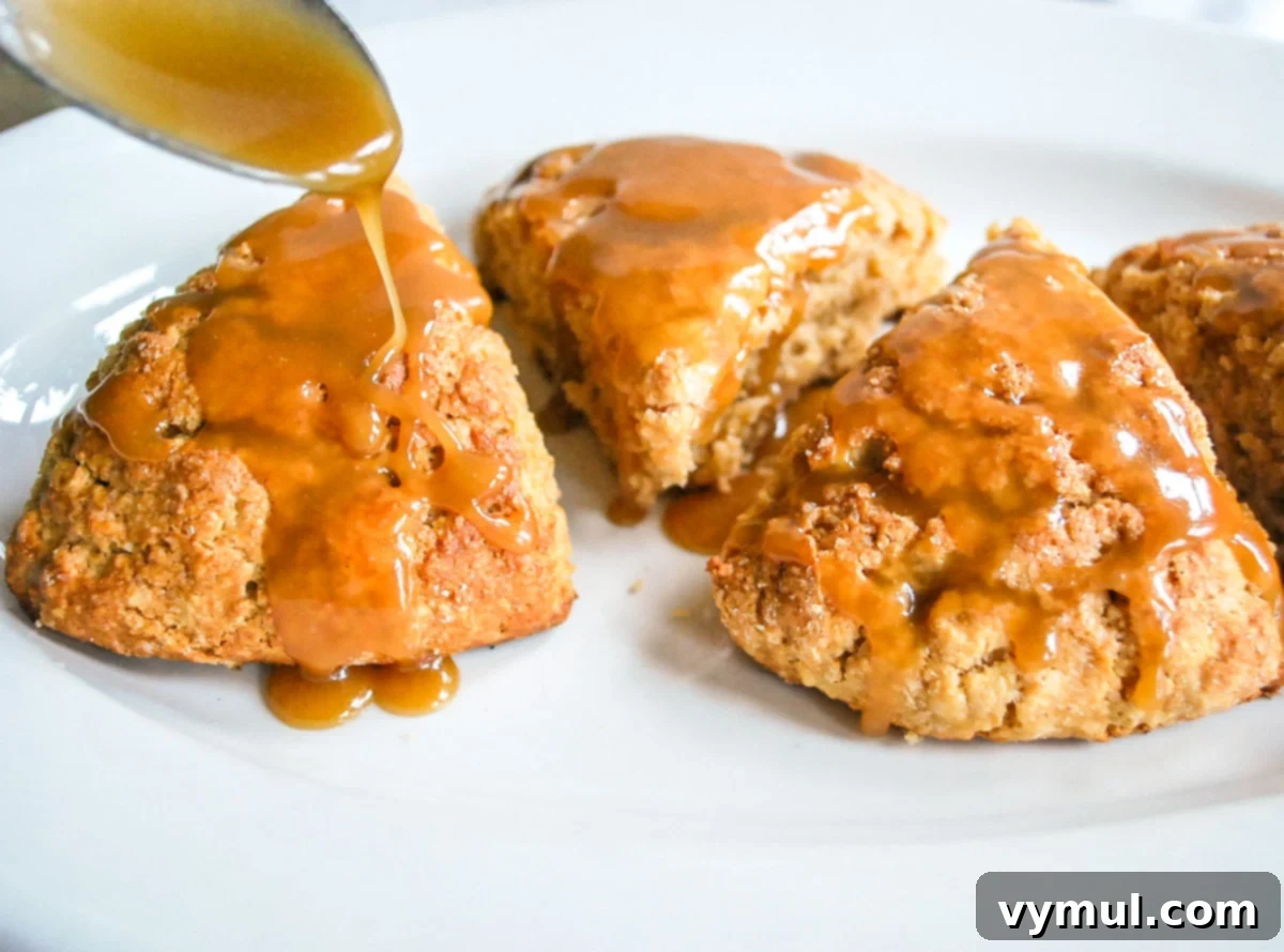 Luscious Double Apple Scones with Golden Caramel Glaze 7 Warm, freshly baked apple scones being drizzled with a rich caramel sauce on a white plate, highlighting their appeal.