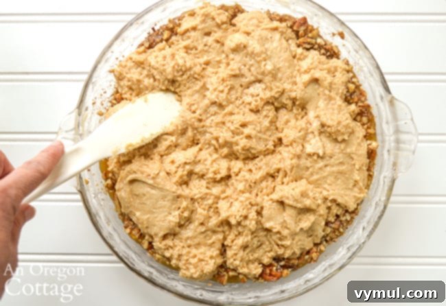 Spoonfuls of sourdough coffee cake batter being spread over the caramel pecan layer in a baking pan.