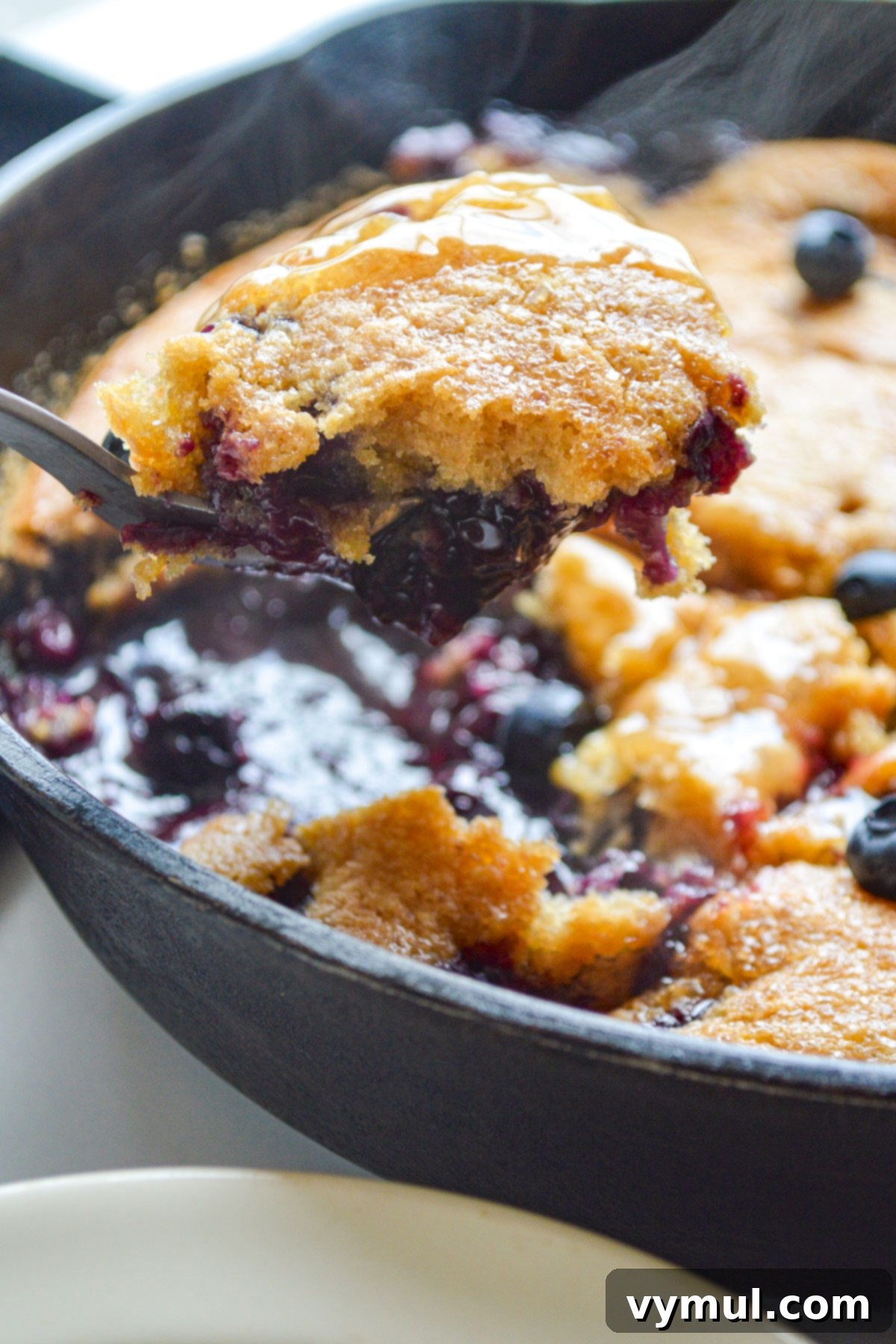 spooning warm blueberry cobbler from skillet