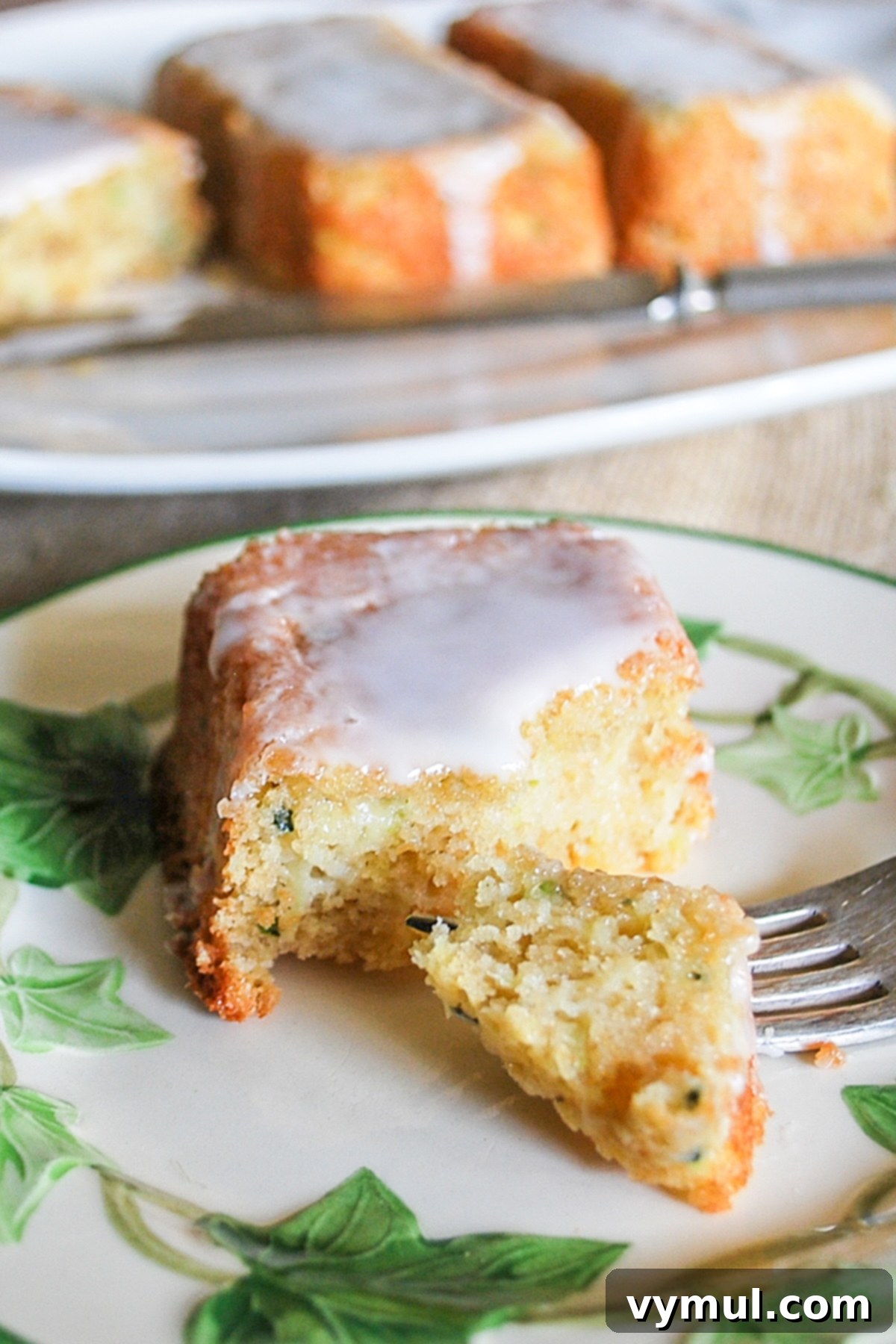 A slice of moist zucchini lemon bread on a plate with a fork, showing the tender crumb and glaze drizzle, ready to be enjoyed as a snack or dessert.