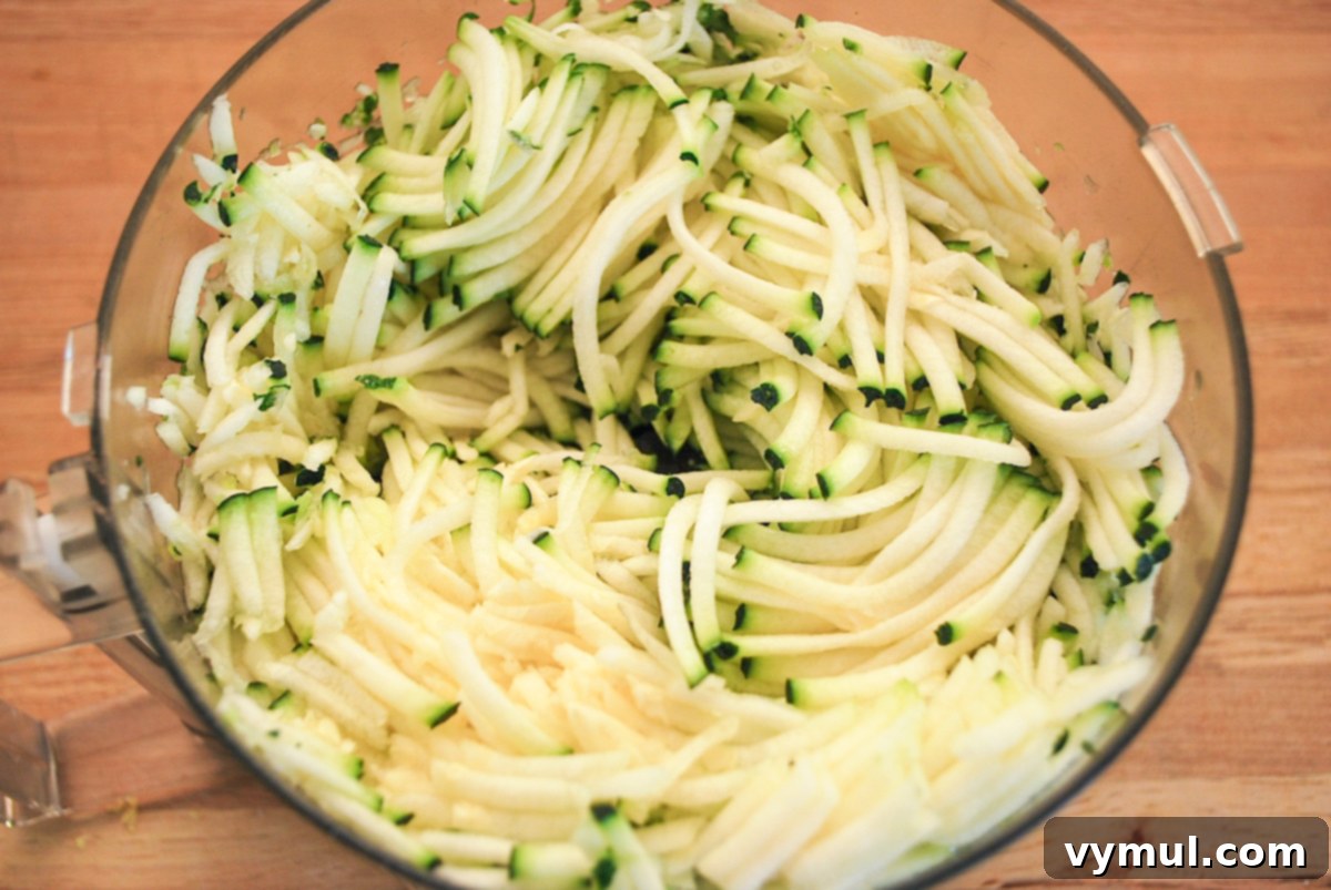 Freshly grated zucchini in a food processor bowl, ready to be added to the lemon bread batter.