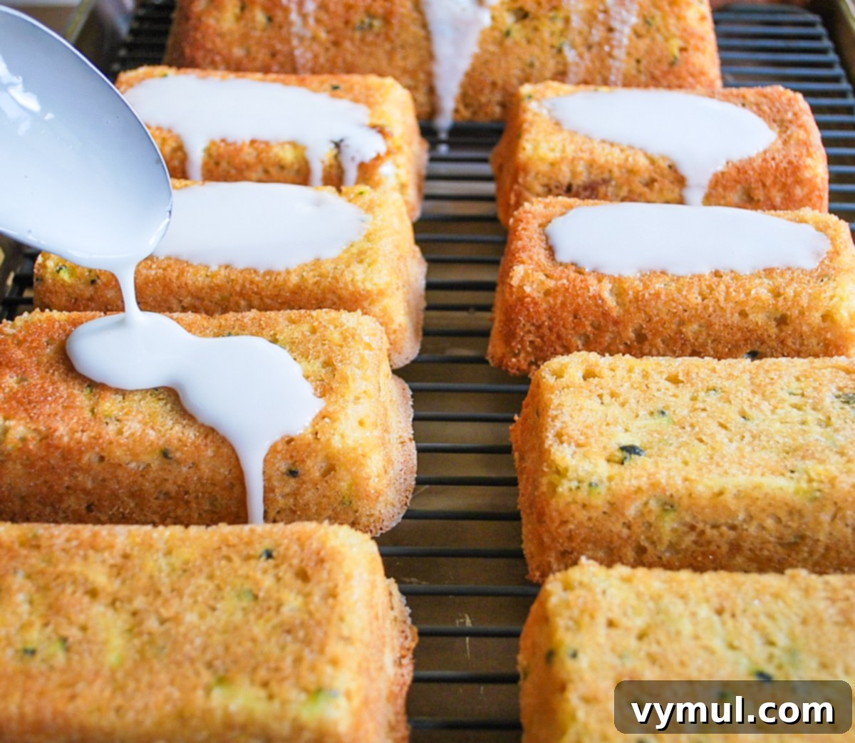 Warm zucchini lemon bread loaves on a cooling rack, being drizzled with a sweet lemon glaze over a baking sheet to catch drips.