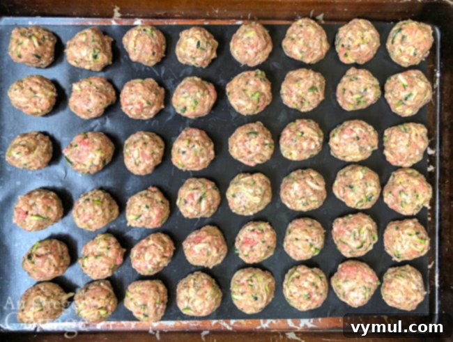 Rows of uncooked zucchini meatballs neatly arranged on a parchment-lined baking sheet, ready for the oven or freezer.