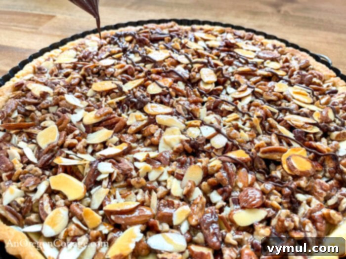 Easy Honey Caramel Triple Nut Tart 7 A hand drizzling melted chocolate over a baked triple nut tart using a piping bag made from a plastic baggie.