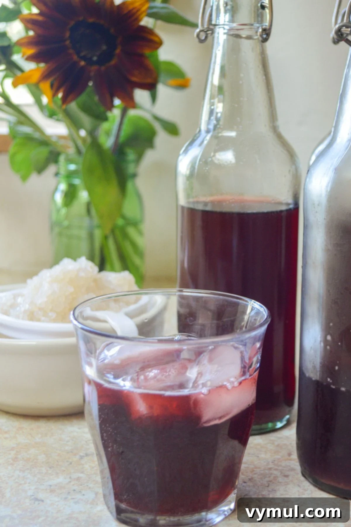 Homemade Water Kefir Made Easy 2 Cherry water kefir in a glass with bottles of fermenting water kefir in the background