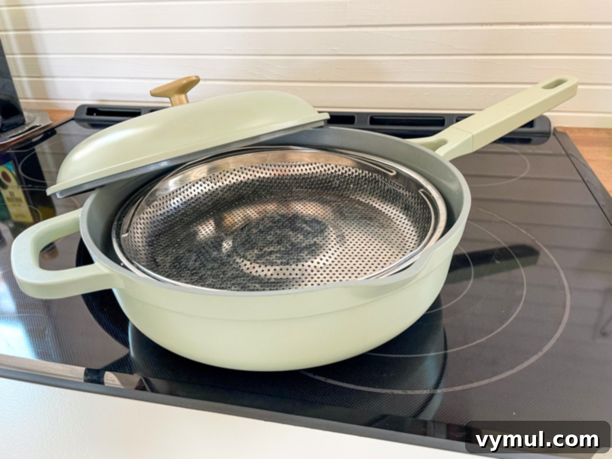 Drew Barrymore's sage green 'Hero Pan' cooking on a stovetop, with a modern and stylish appearance.