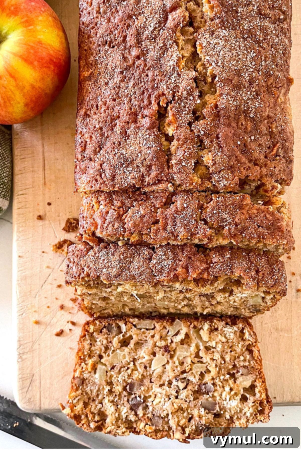 Easy Wholesome Honey Cinnamon Apple Oat Loaf 2 Sliced loaf of healthy cinnamon oat apple bread on a cutting board, with whole apples in the background