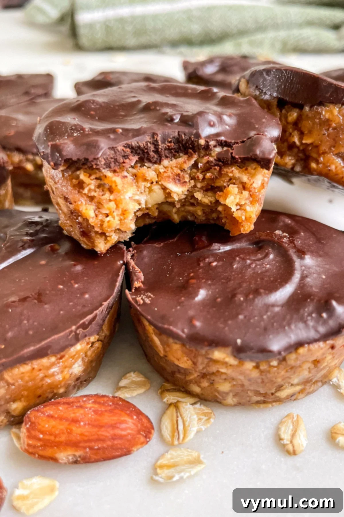 Stacked no-bake chocolate almond oat cups with one featuring a delicious bite taken out, highlighting the rich chocolate topping and wholesome oat base.