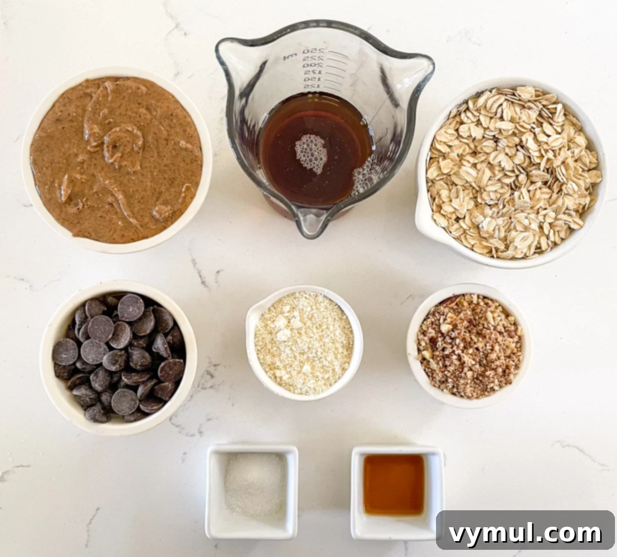 Assorted ingredients for no-bake chocolate almond oat cups laid out on a surface, including oats, almond flour, maple syrup, and chocolate chips.