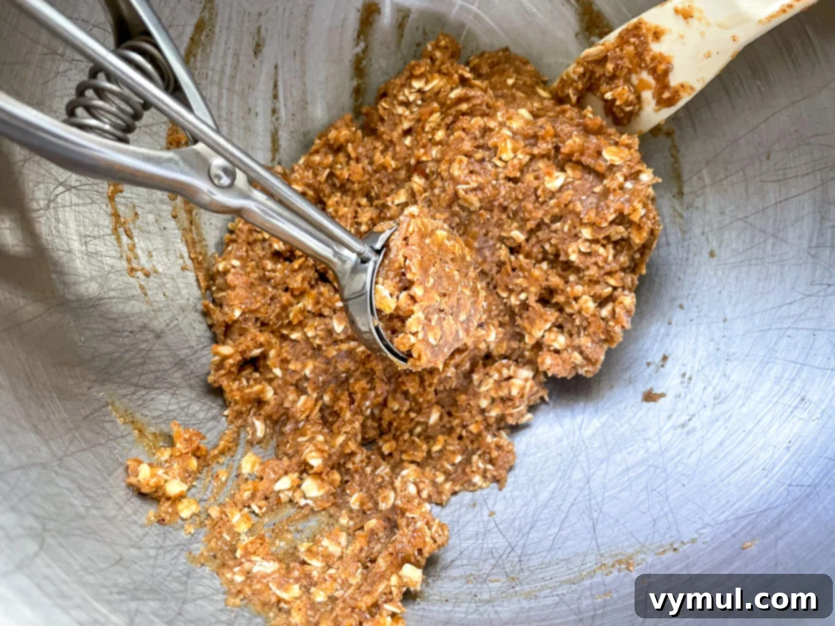 A scoop of mixed dough for the no-bake oat cups being transferred to a muffin tin, ready to be pressed into shape.