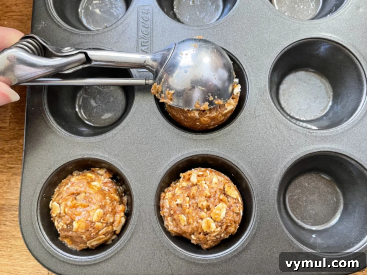 Using a tablespoon scoop to portion the no-bake chocolate almond oat cup dough into a mini muffin tin for consistent sizing.