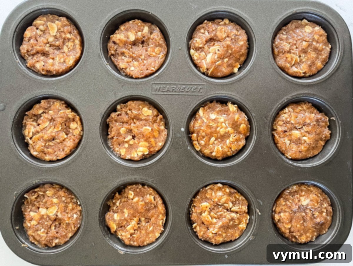 A mini muffin tin filled with firmly pressed no-bake chocolate almond oat cup dough, ready for freezing.