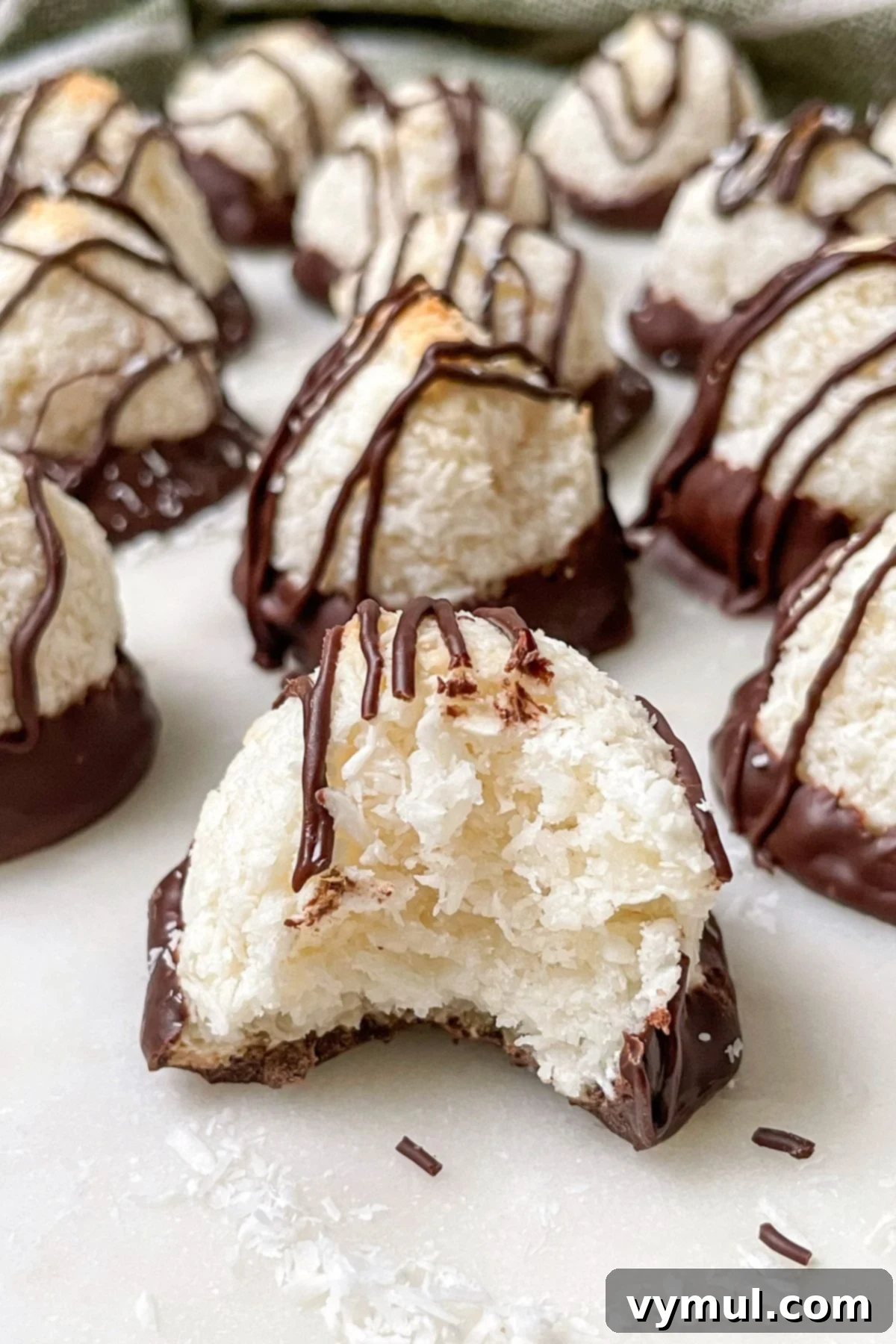 Effortless Coconut Macaroons No Flour No Condensed Milk 2 Delightful coconut macaroons neatly arranged on a pristine white marble surface, with one cookie showing a perfect bite taken out, highlighting its chewy interior and golden exterior.