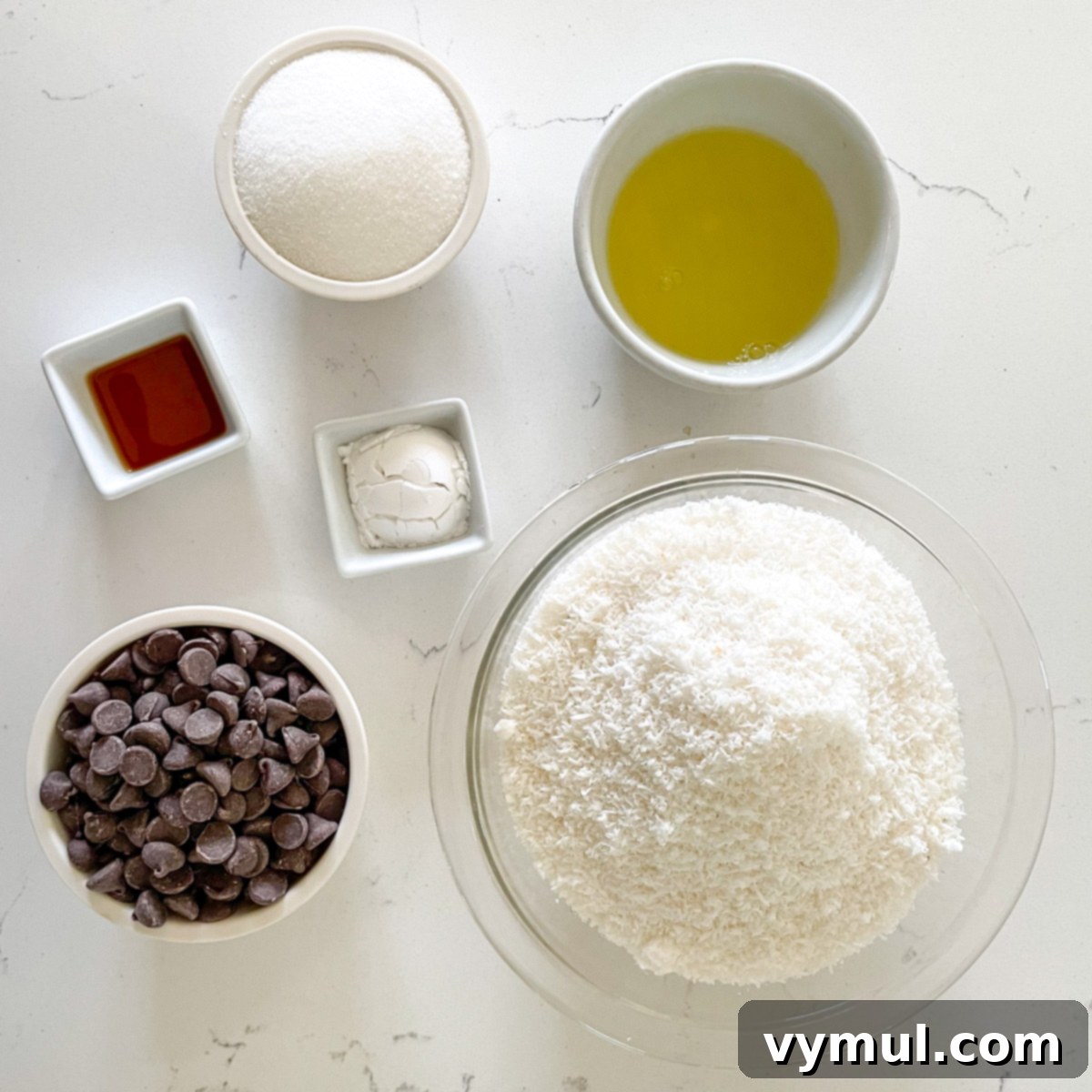 Effortless Coconut Macaroons No Flour No Condensed Milk 3 A top-down view showing the simple ingredients laid out for making coconut macaroons: unsweetened shredded coconut, sugar, potato starch, egg whites, vanilla extract, and dark chocolate chips.