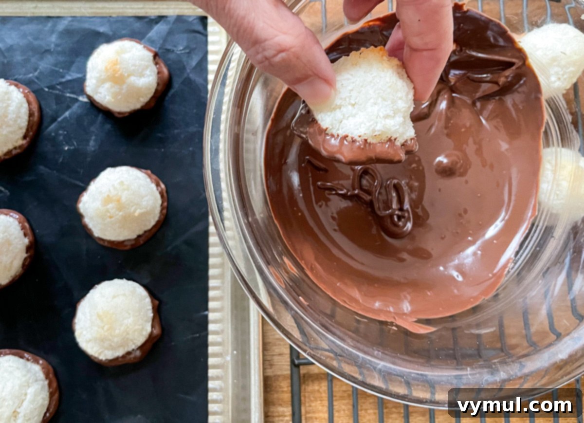 Effortless Coconut Macaroons No Flour No Condensed Milk 6 Close-up shot of a coconut macaroon being dipped into melted dark chocolate, coating its base for an irresistible finish.