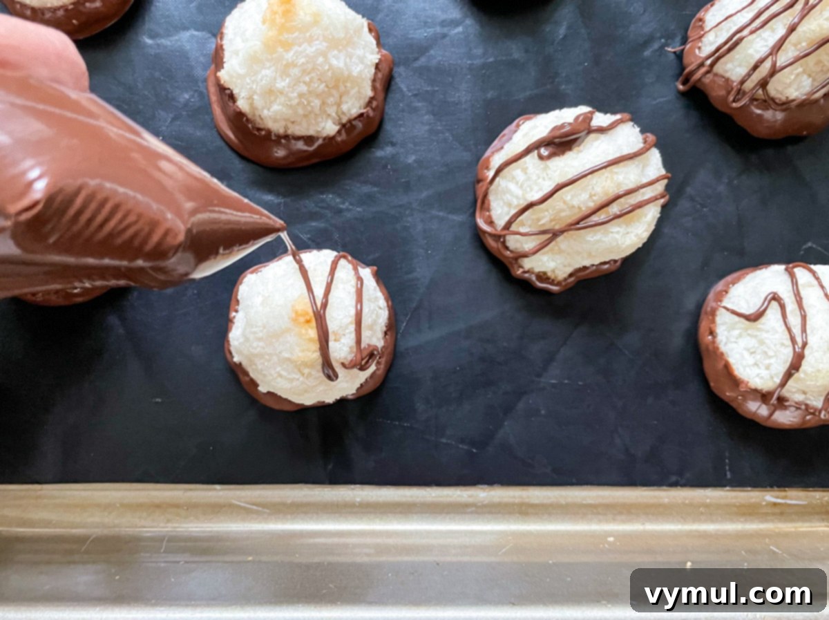 Effortless Coconut Macaroons No Flour No Condensed Milk 7 Melted chocolate being artfully drizzled over the tops of already chocolate-dipped coconut macaroons, adding an extra layer of gourmet appeal.