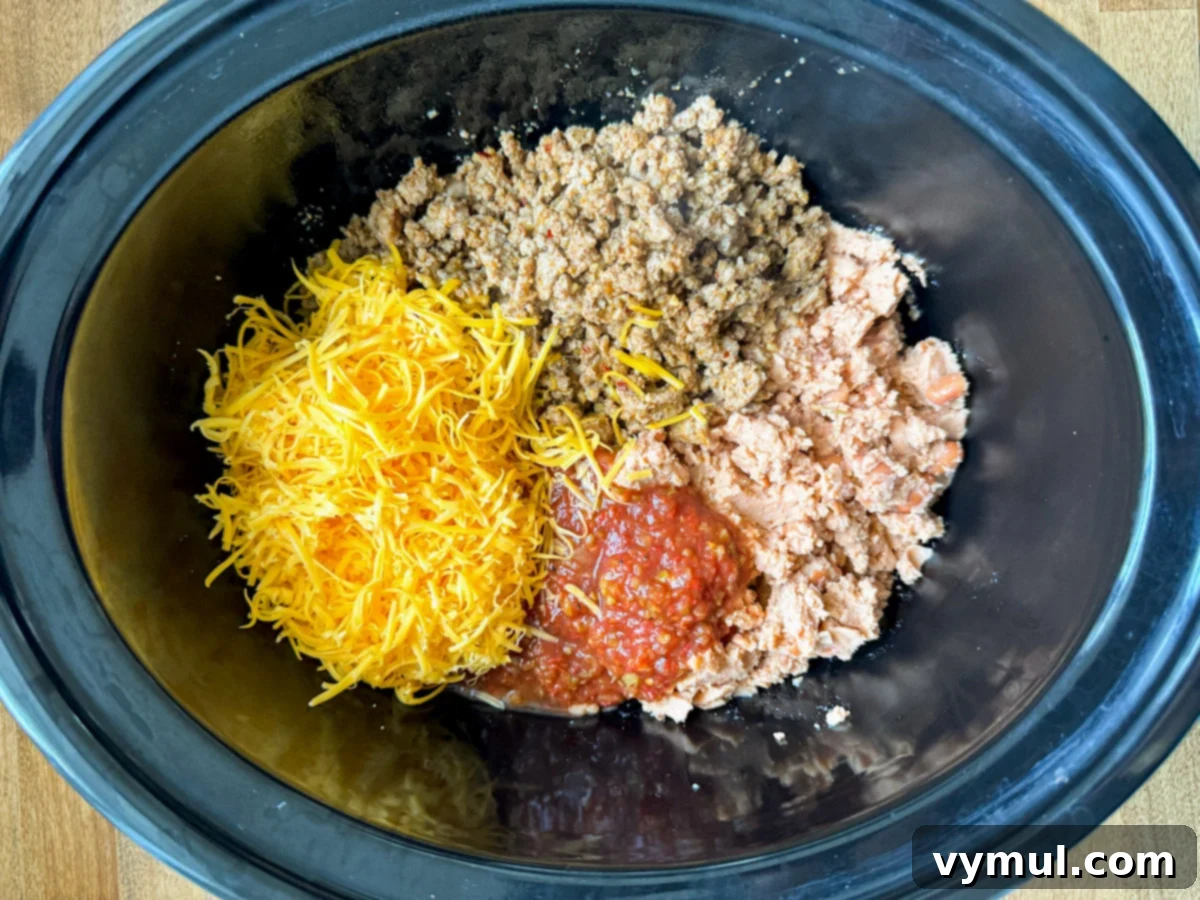 Hands-Off 5-Ingredient Taco Dip for Slow Cooker and Instant Pot 5 Adding all remaining ingredients, including browned meat, refried beans, salsa, and cheese, into the slow cooker insert.