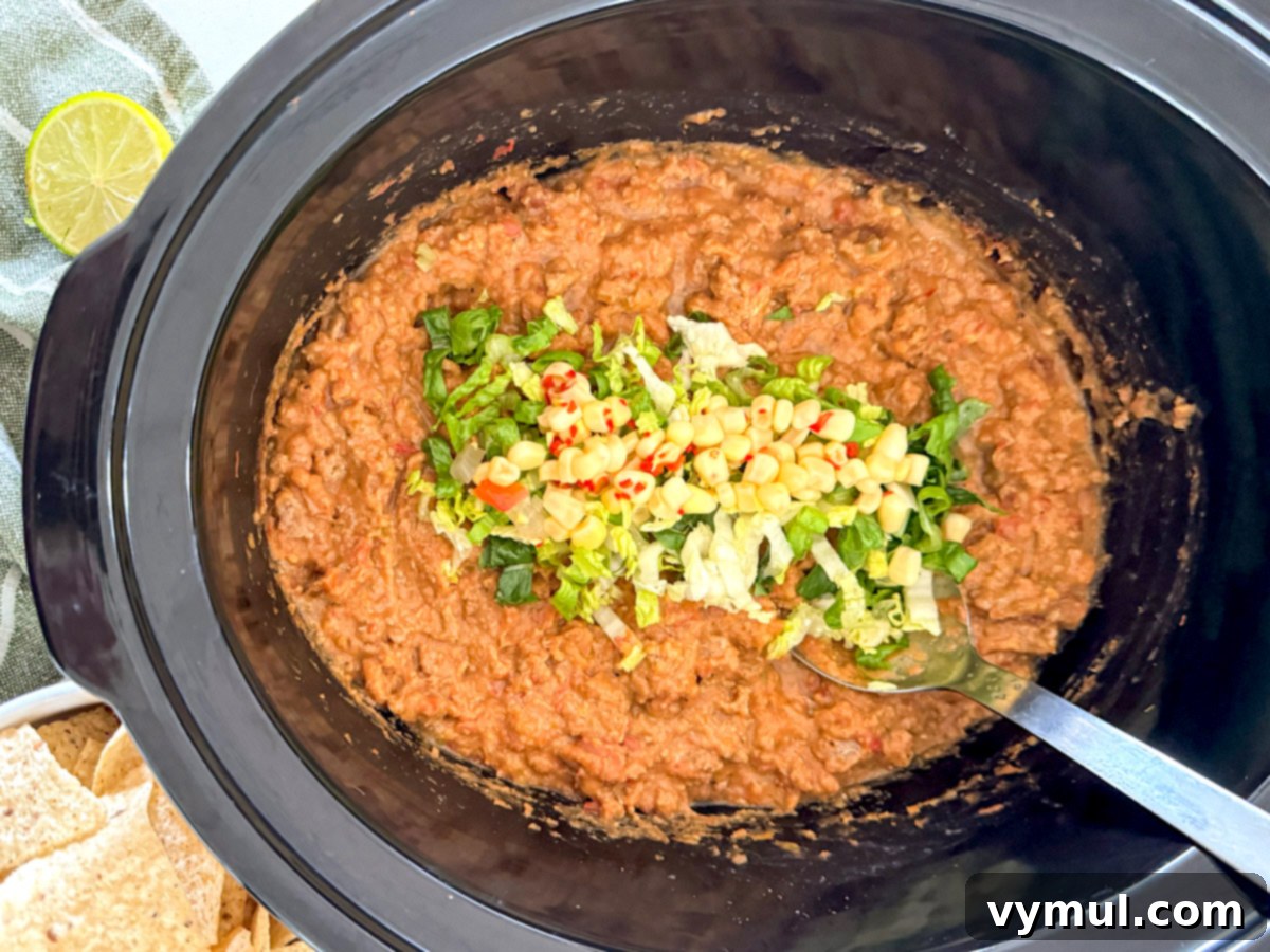 Hands-Off 5-Ingredient Taco Dip for Slow Cooker and Instant Pot 7 Adding fresh toppings such as shredded lettuce, corn relish, and salsa to the finished slow cooker taco dip in the black bowl.