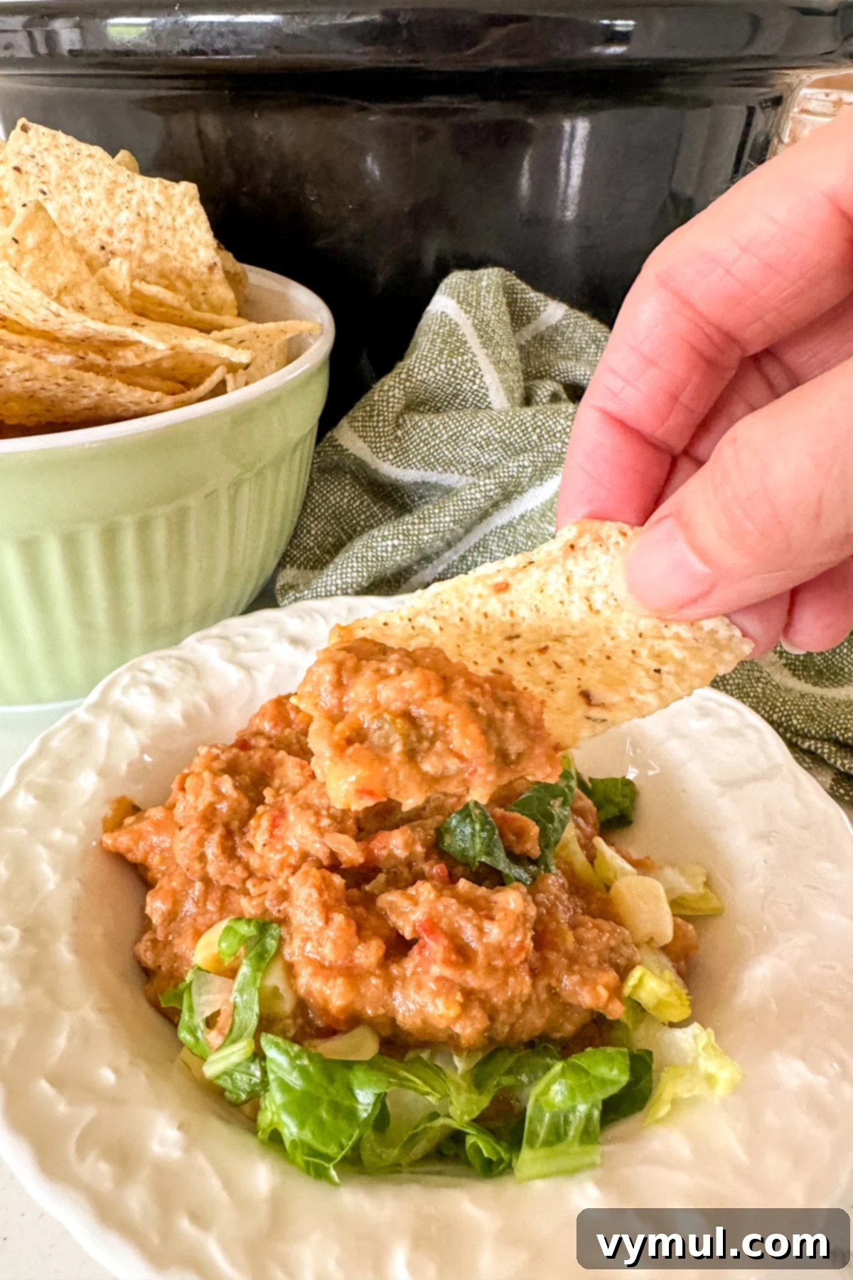 Hands-Off 5-Ingredient Taco Dip for Slow Cooker and Instant Pot 8 A close-up shot of a tortilla chip loaded with slow cooker taco dip and fresh toppings, ready to be enjoyed.