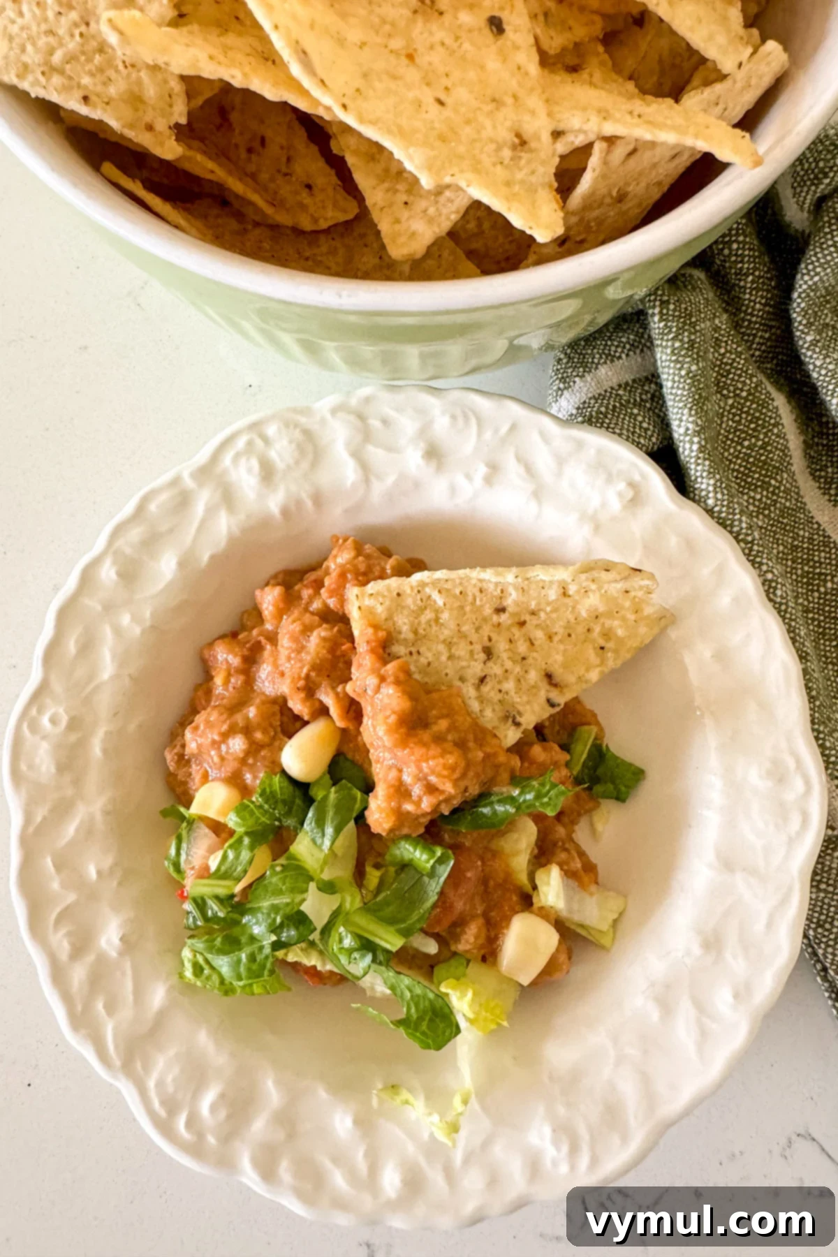 Hands-Off 5-Ingredient Taco Dip for Slow Cooker and Instant Pot 9 A small white bowl filled with creamy slow cooker taco dip, surrounded by tortilla chips, ready for dipping.