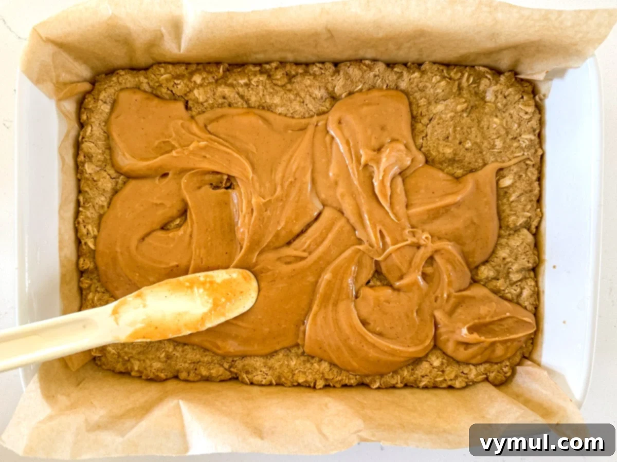 Step 5: The peanut butter and condensed milk filling is being spread gently over the partially baked oat crust.