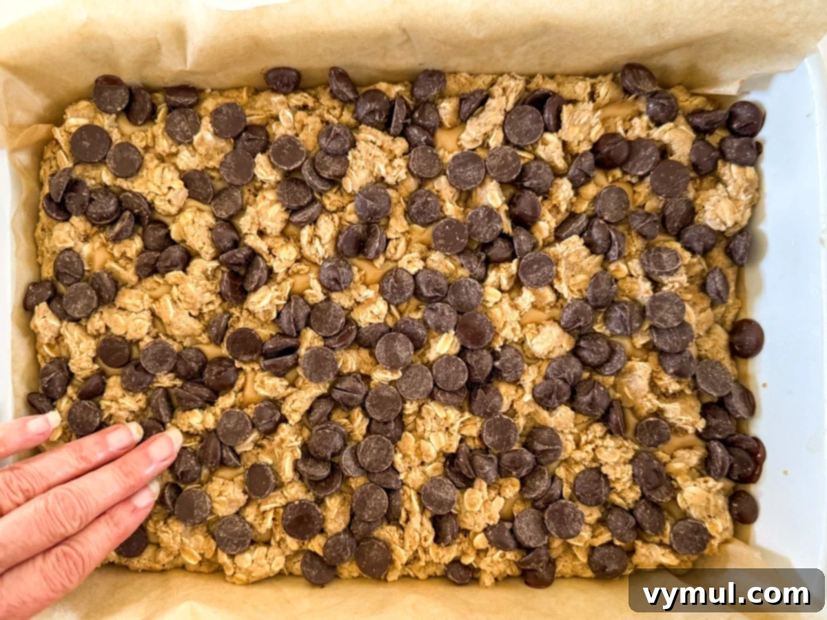 Step 6: The reserved oat crumble and chocolate chips are sprinkled over the peanut butter layer, ready for final baking.