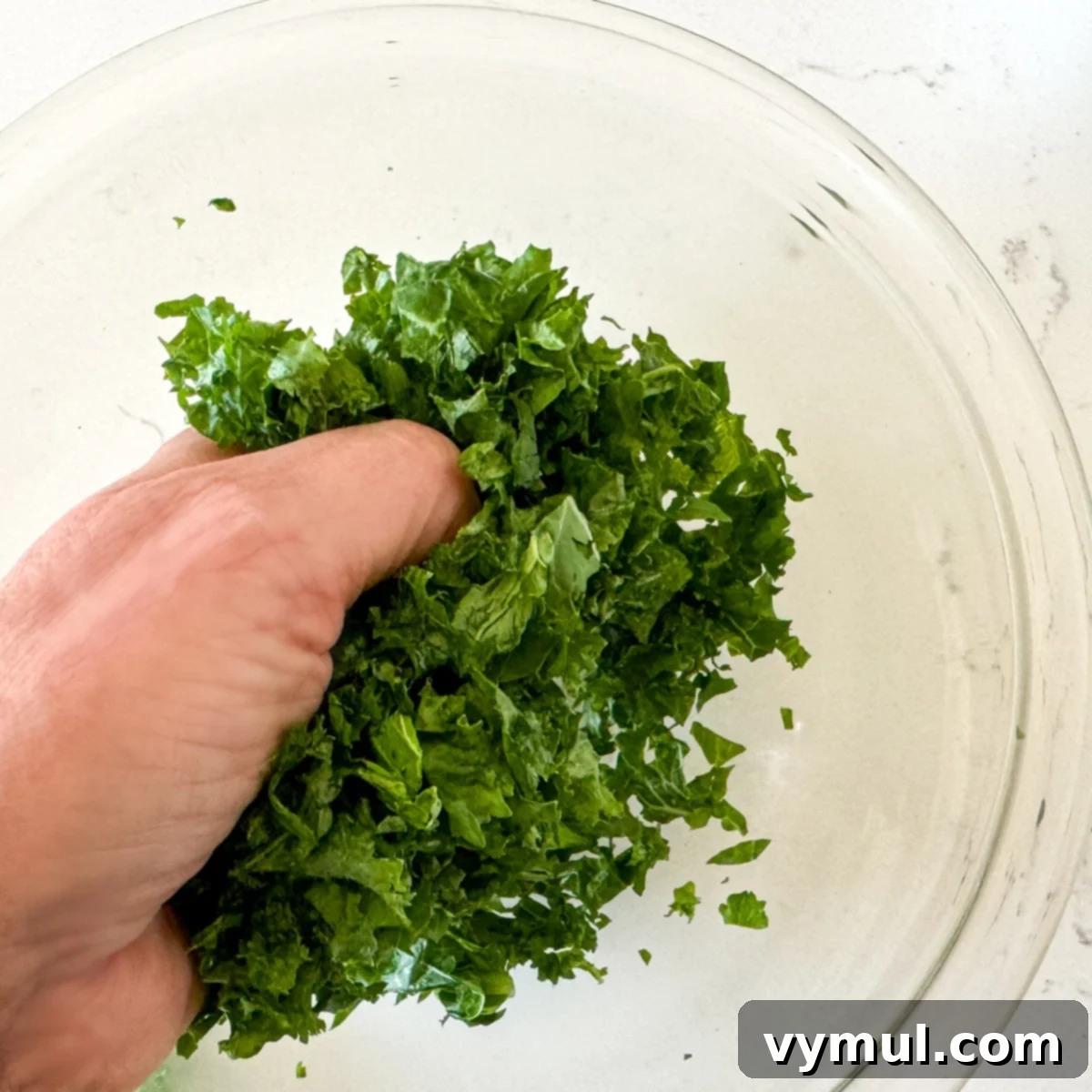 Zesty Lemon and Parmesan Kale Quinoa Salad 5 Hands massaging chopped kale in a medium bowl.