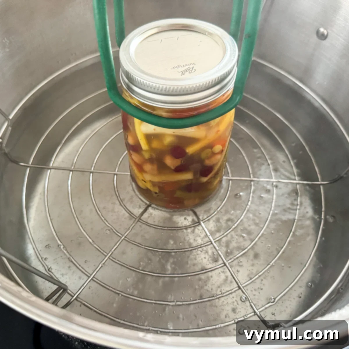 Adding a freshly filled canning jar of three bean salad to a simmering water bath canner.