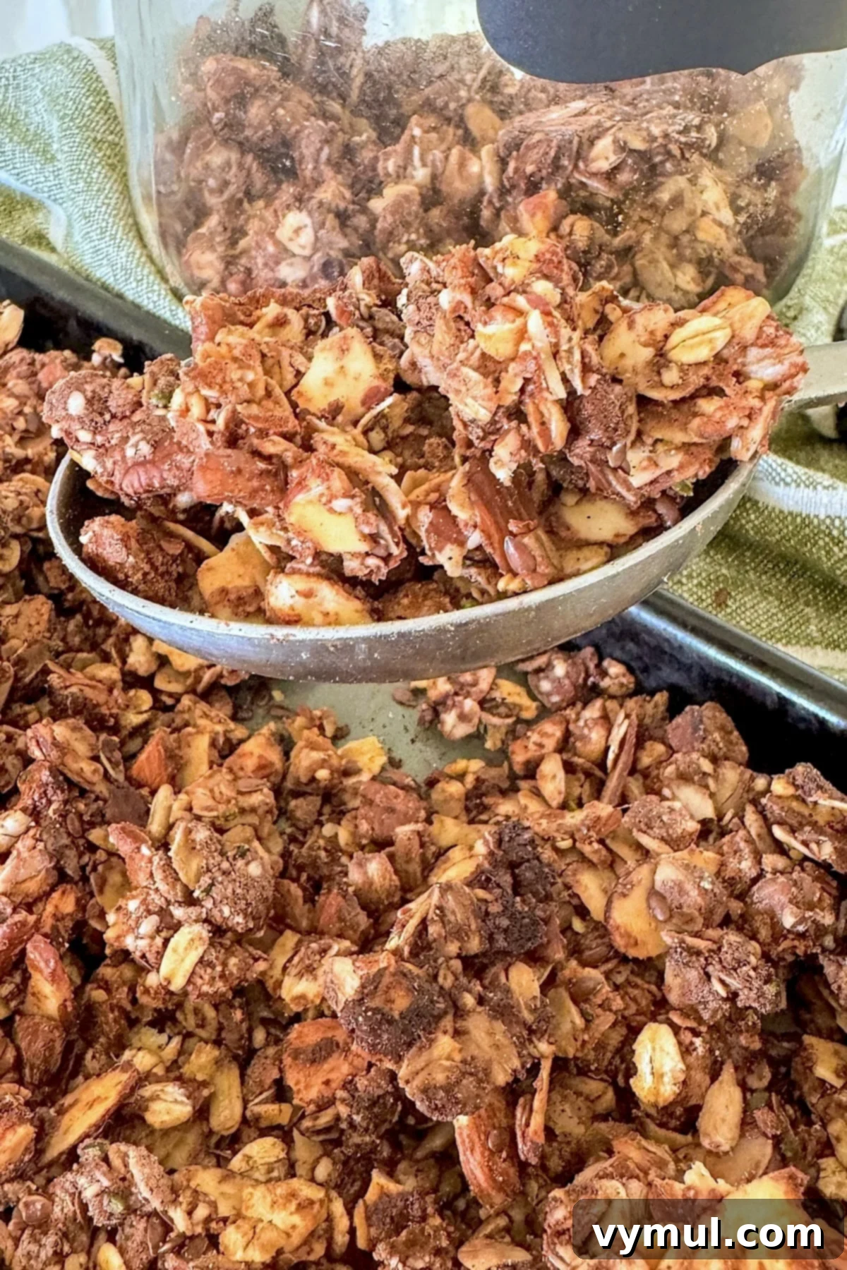 Breaking up baked high-protein maple cinnamon granola into clusters and transferring it to a clear glass storage jar for freshness.