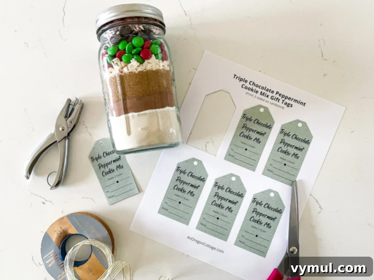 Triple Chocolate Peppermint Cookie Jar Mix with Printable Tags 4 A charming arrangement of a chocolate peppermint cookie mix jar, decorative tags, ribbon, and scissors, ready for gifting.