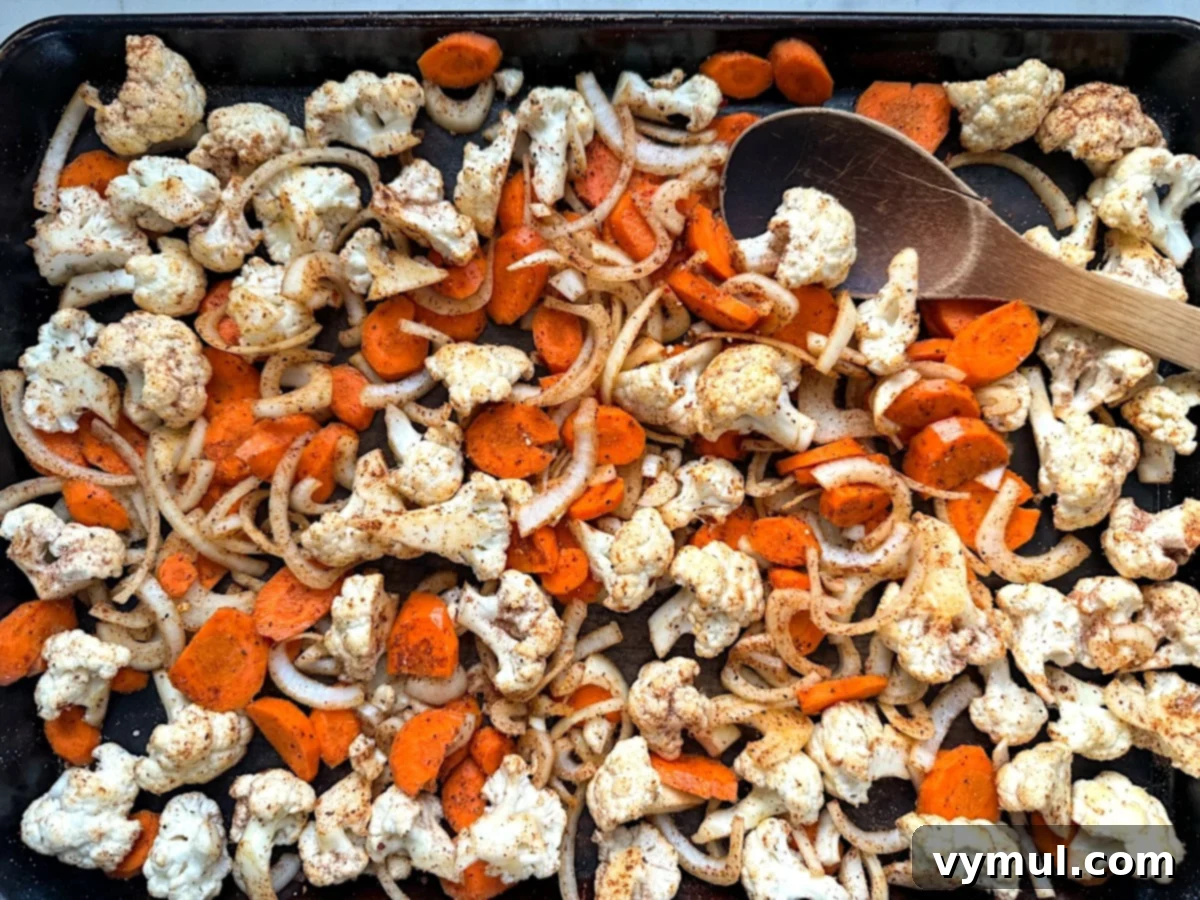 Simple Healthy Chili Roasted Cauliflower and Carrots 5 mixing vegetables on baking sheet with wood spoon