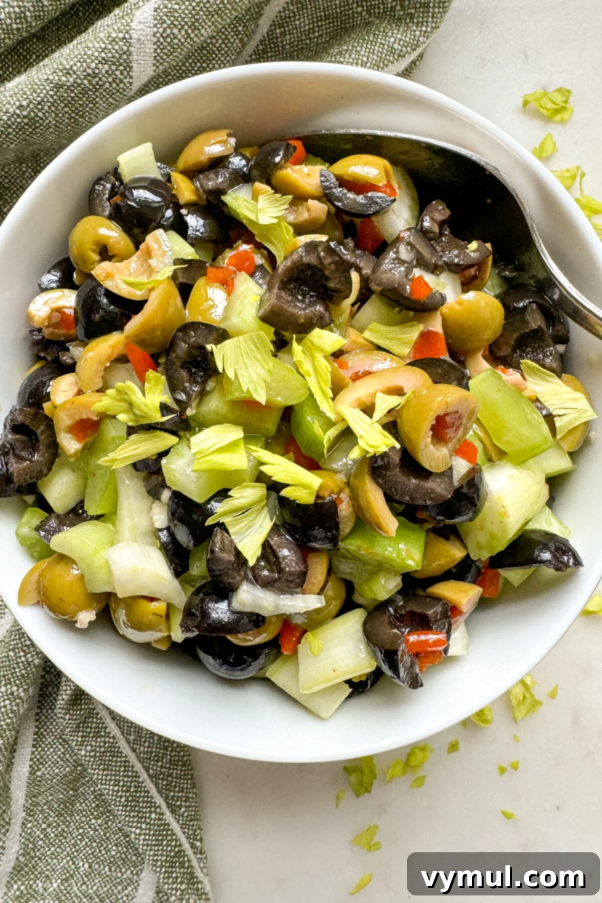 Effortless Olive Salad, Maximum Flavor 2 A vibrant olive salad, featuring green and black olives, celery, and herbs, presented in a pristine white bowl from a top-down perspective, ready to be enjoyed as a versatile topping or side dish.