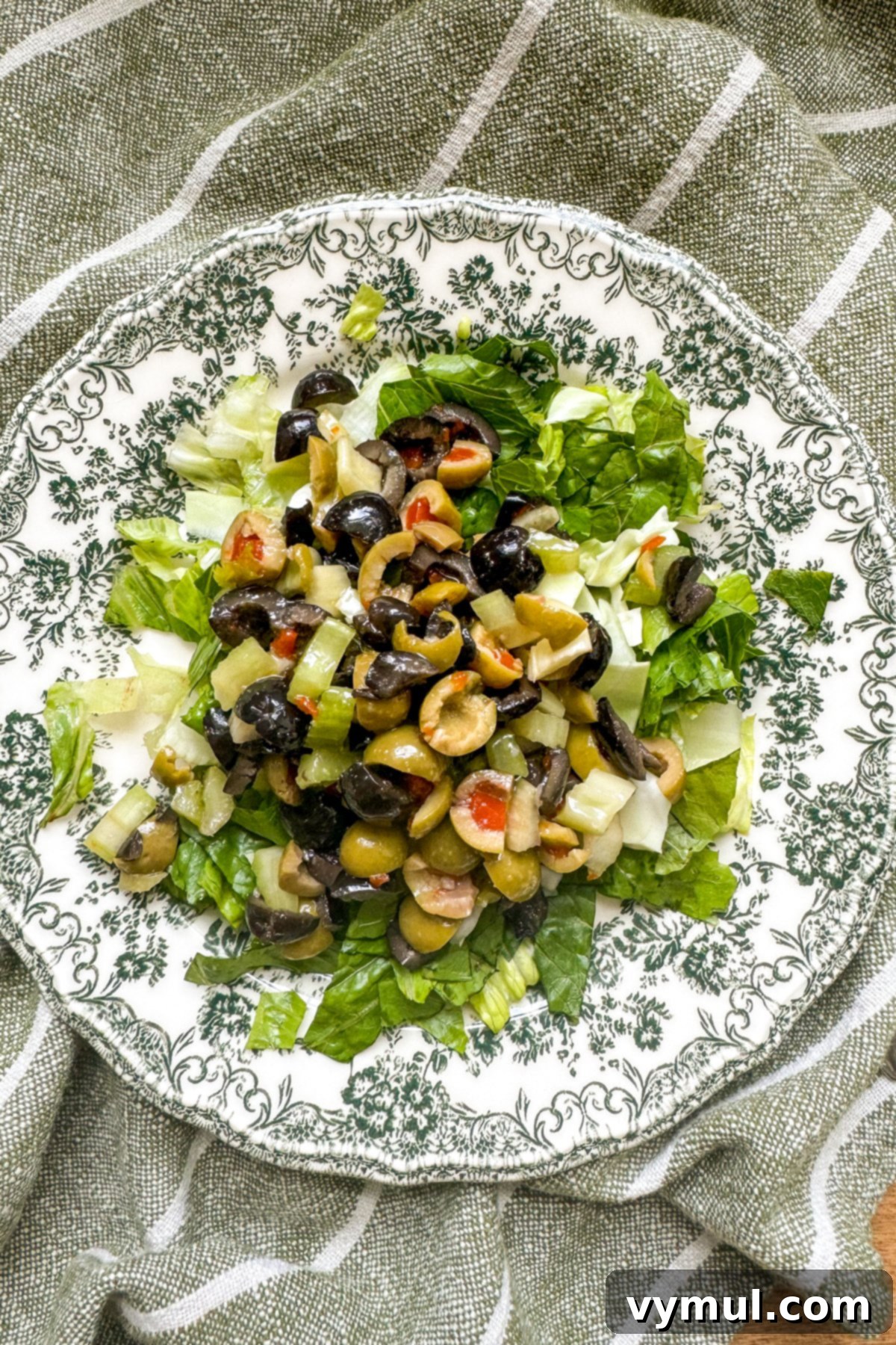 Effortless Olive Salad, Maximum Flavor 6 Olive salad generously spooned over a bed of crisp lettuce on a green floral plate, showcasing its potential as a fresh and flavorful salad topping.