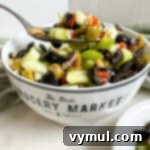 Effortless Olive Salad, Maximum Flavor 7 A spoon delicately scooping olive salad from a white bowl, illustrating the salad's texture and readiness for serving.