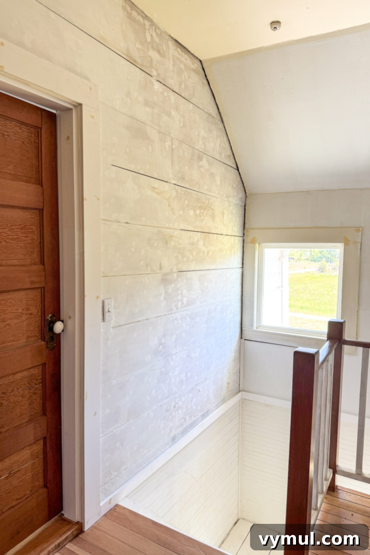 Farmhouse stairwell during renovation, showing exposed wood walls and restored elements.