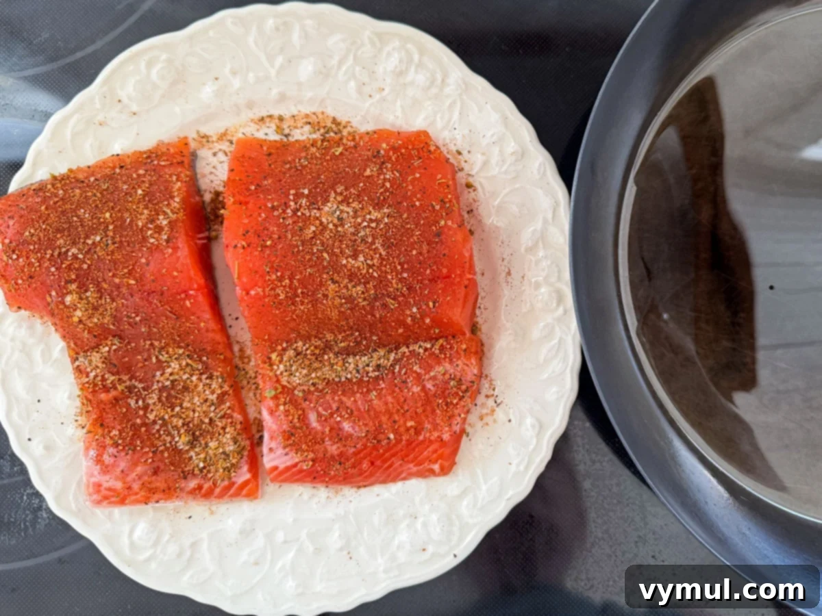 Perfect Pan-Seared Salmon Caesar 8 Two seasoned salmon fillets on a plate, ready to be pan-seared next to a hot skillet.