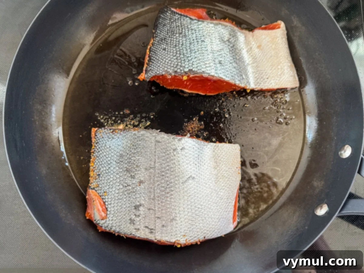 Perfect Pan-Seared Salmon Caesar 9 Salmon fillets searing skin-side up in a hot pan, developing a dark, flavorful crust.
