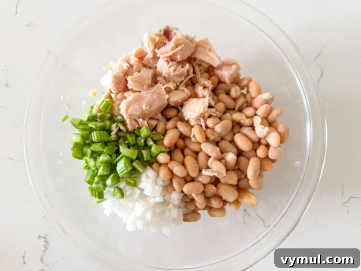 Pantry Powerhouse Protein Chicken Salad 4 Main ingredients for chicken salad, including shredded chicken, drained white beans, and diced vegetables, in a mixing bowl.