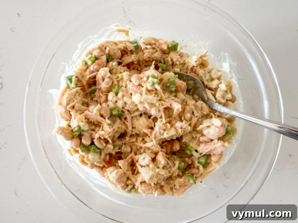 Pantry Powerhouse Protein Chicken Salad 6 Creamy dressing being mixed into the chicken salad ingredients in a bowl.
