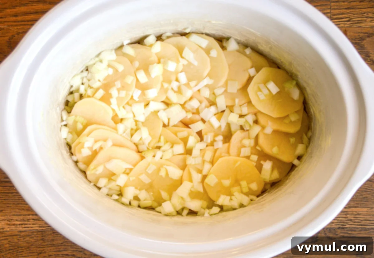 Irresistible Slow Cooker Cheesy Garlic Scalloped Potatoes 5 first layer of potatoes and onions in slow cooker
