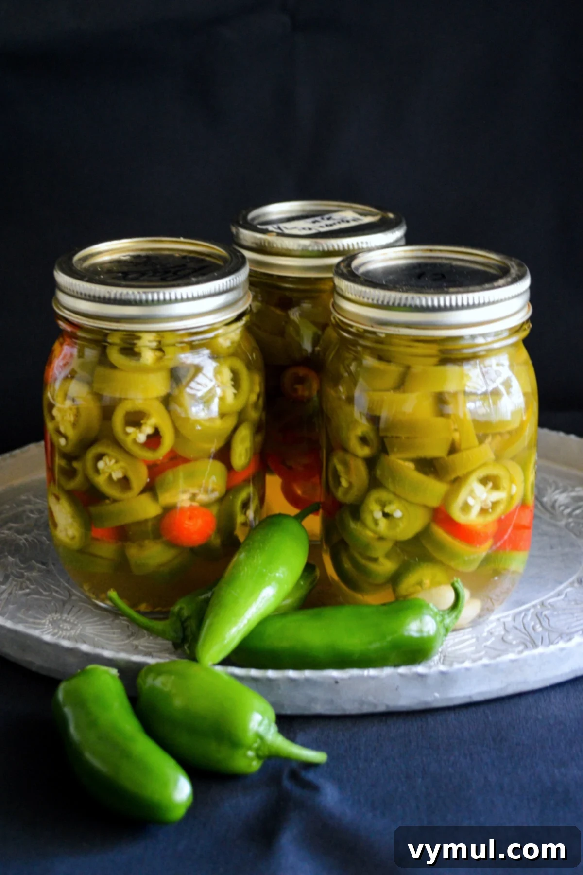 jars of sliced quick pickled jalapeños on a tray with black background