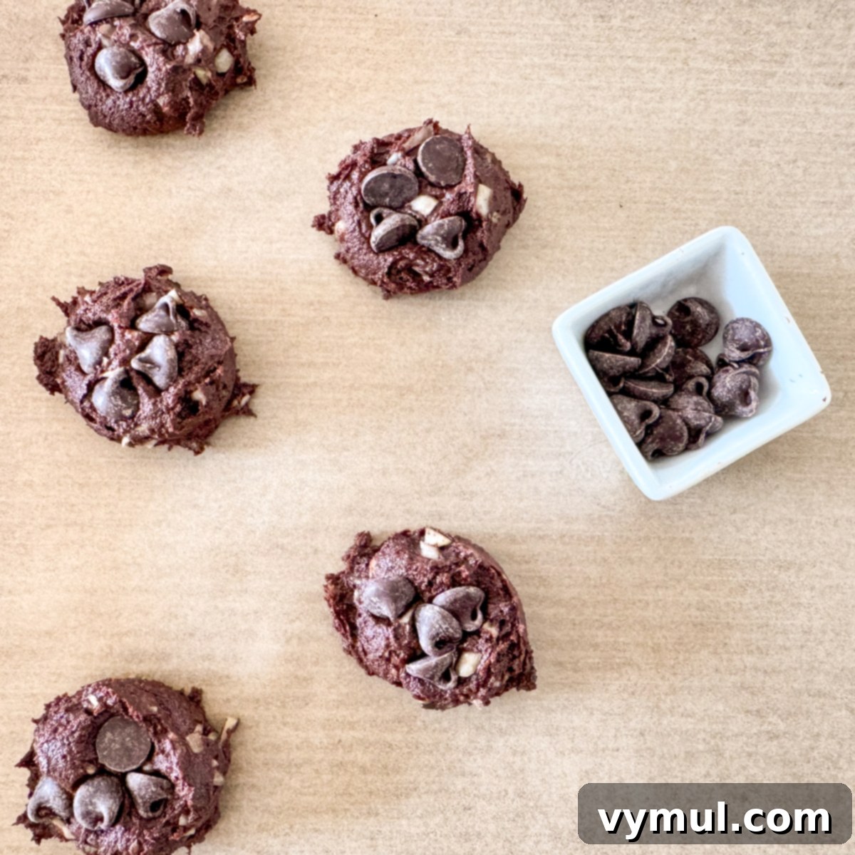 Portioning chocolate zucchini cookie dough onto a parchment-lined baking sheet and adding chocolate chips