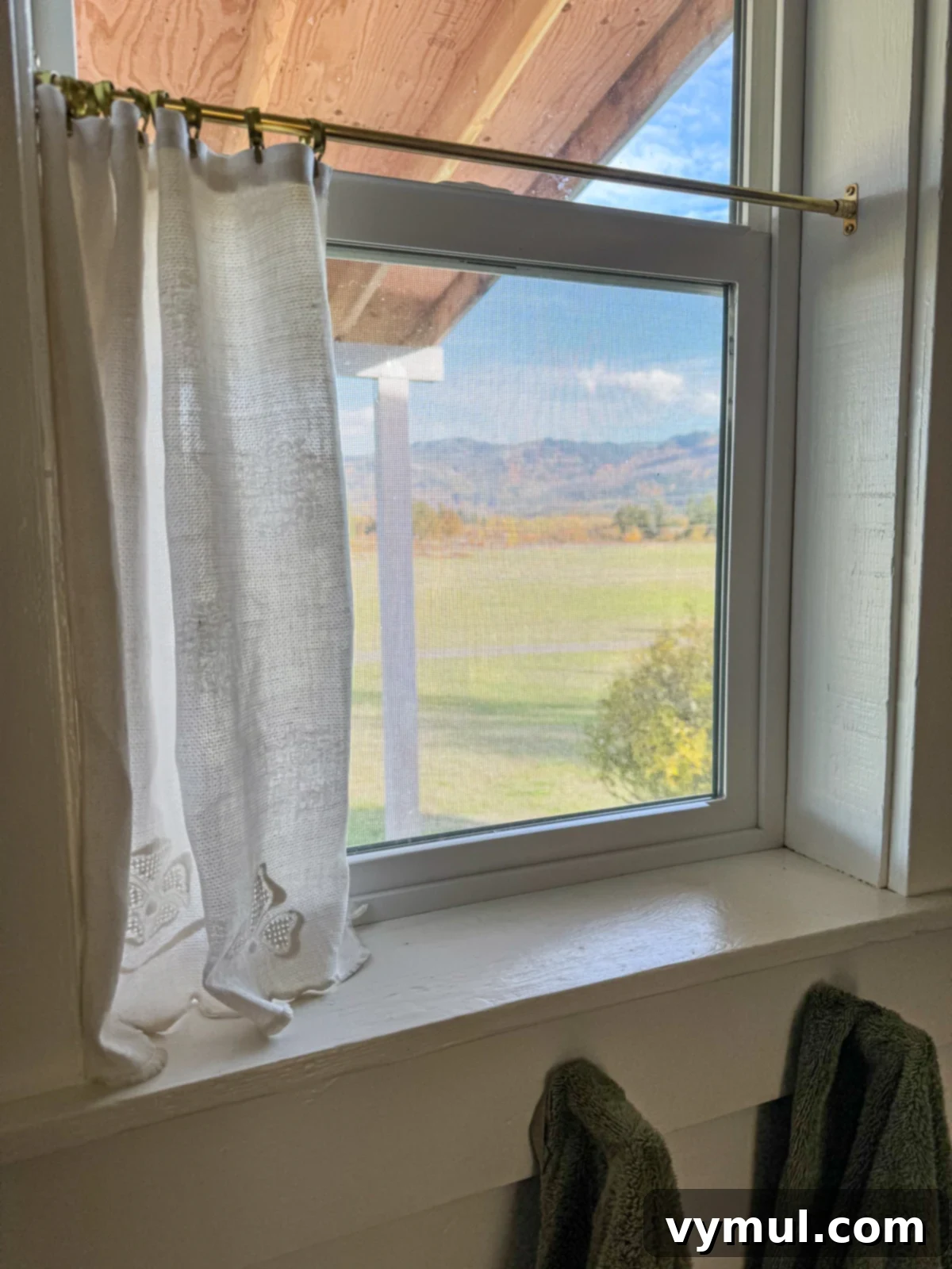 Vintage linen cafe curtain in the bathroom, elegantly pulled open to reveal the outside view