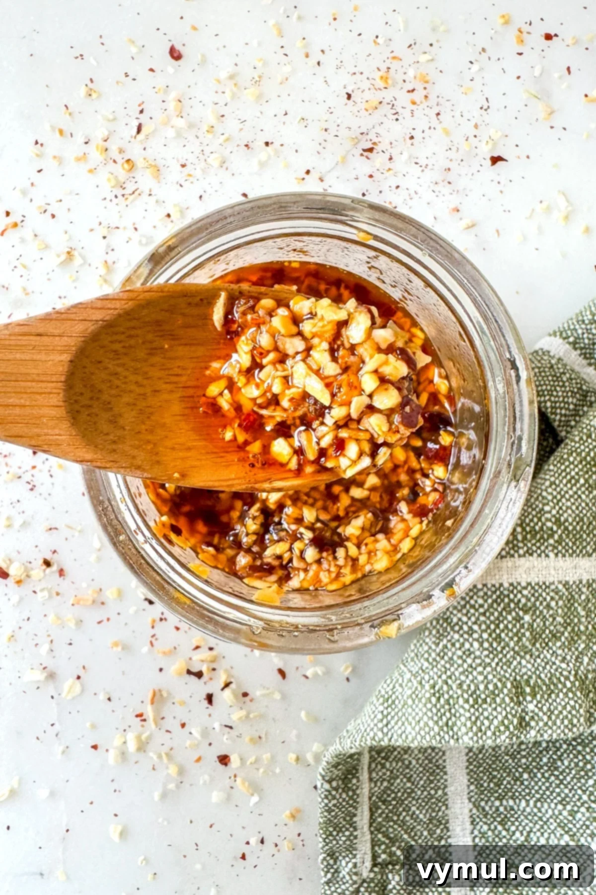 Homemade chili crisp on a wooden spoon over a jar, showcasing its vibrant red color and crunchy texture