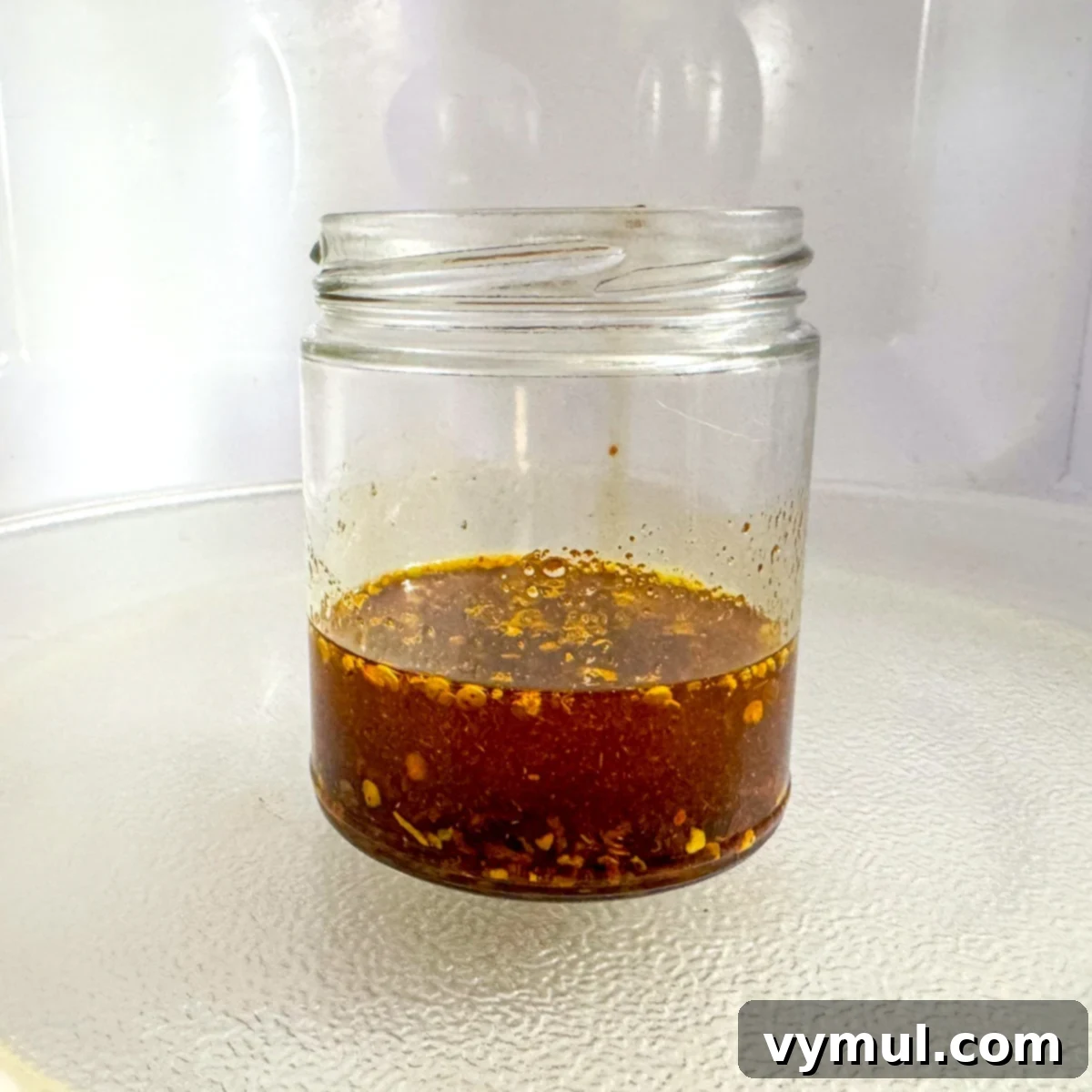Glass jar with chili crisp ingredients being microwaved