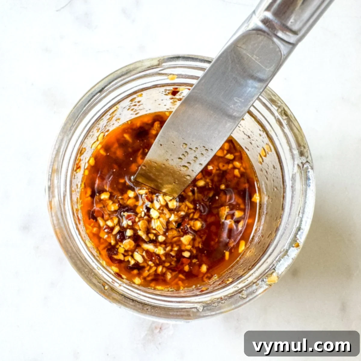 All chili crisp ingredients being mixed together in a glass jar after heating