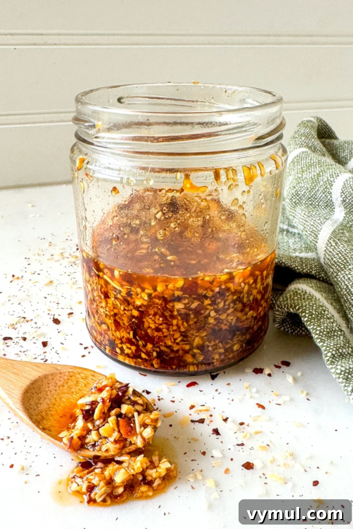 A jar of homemade chili crisp with a wooden spoon resting on top, laden with crunchy chili oil